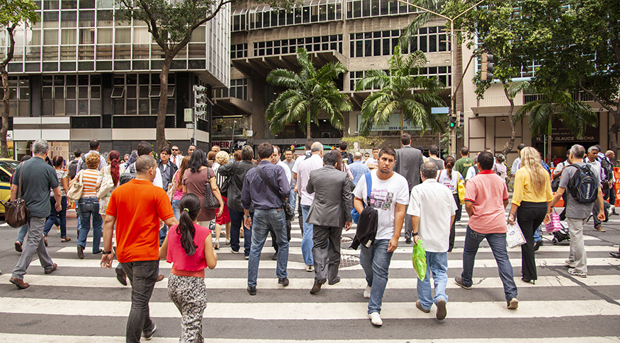 #PraCegoVer A foto mostra pessoas atravessando uma rua movimentada, no Centro do Rio de Janeiro
