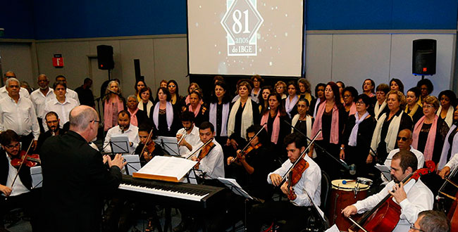 galeria-1 #PraCegoVer maestro de costas no centro da imagem e coral ao fundo