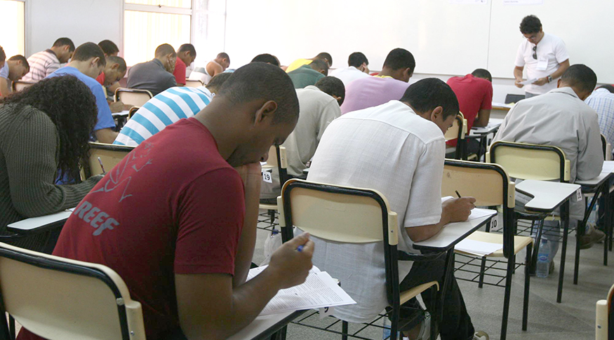 #PraCegoVer A foto mostra um grupo de pessoas em sala de aula. fazendo prova de concurso