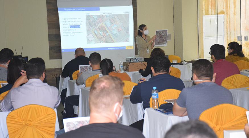 #Pracegover A foto mostra um auditório cheio e uma pessoa fazendo uma palestra